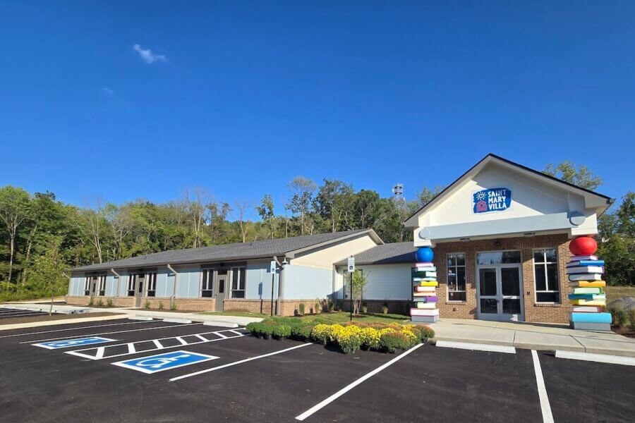 This Nashville Mom Rebuilt Her Life at Renewal House - 4 A single-story building with a “Saint Mary Villa” sign, decorative entrance pillars, accessible parking spaces, and landscaped greenery in front—near Renewal House—set against a background of trees and blue sky.