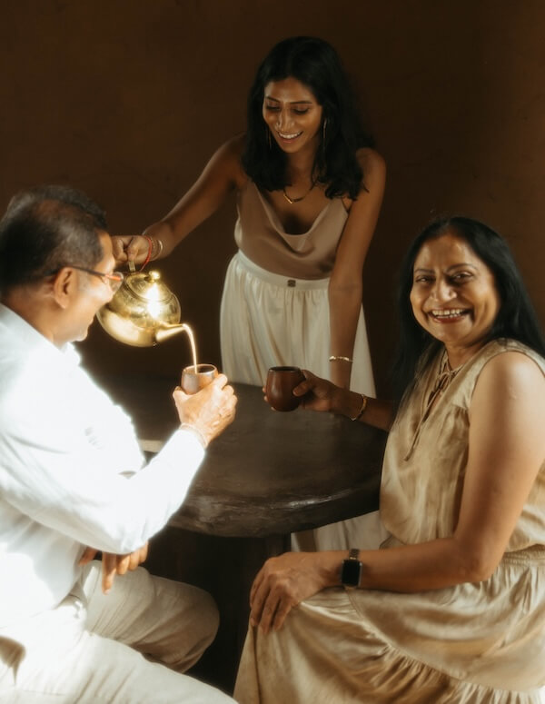 She's Behind Nashville's Dreamiest Coffee Shop - 4 At Cafe Babu, Shivani Darsinos pours tea from a brass teapot for an older man and woman seated at a round table; all three are smiling.