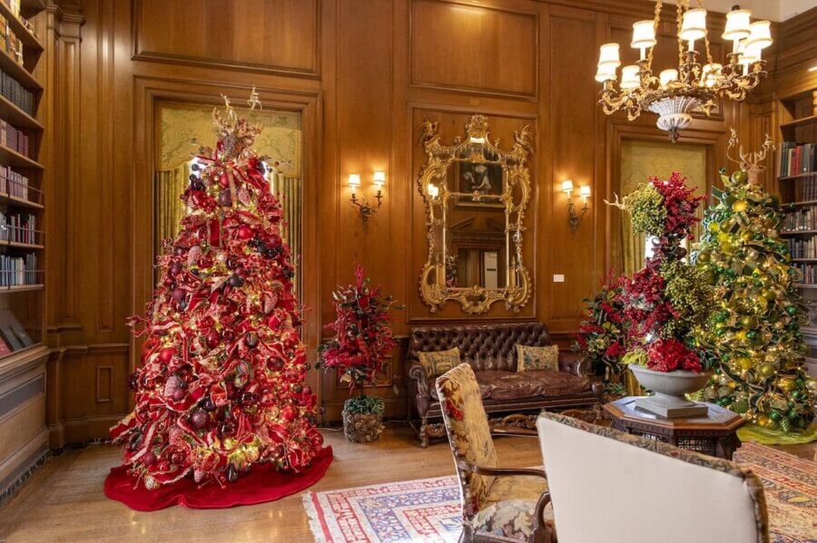 30+ Nashville Holiday Pop-Ups to Get You in the Spirit! - 3 A wood-paneled library in Nashville, decorated for the holiday season with two large Christmas treesβone red and one greenβadorned with ornate ornaments and festive lights, surrounded by classic furniture and bookshelves.