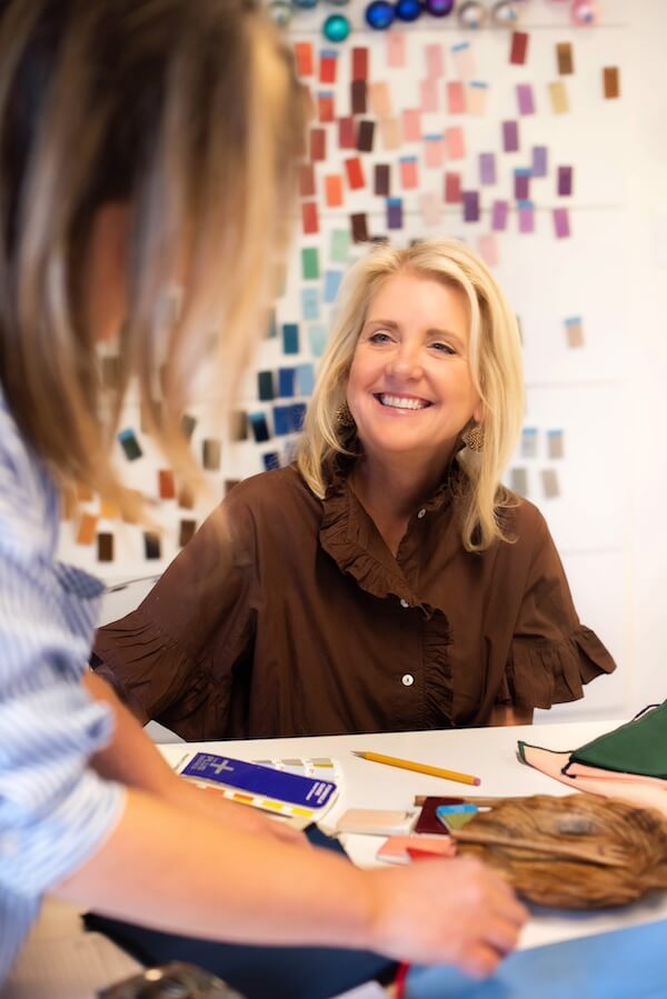 Happy Everything! Laura Johnson’s Joyful Approach to Home & Hosting - 4 Laura Johnson and a colleague sit at a table discussing materials, with color swatches on the wall in the background. Laura is smiling, bringing a touch of Happy Everything to their creative conversation.