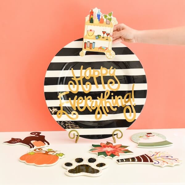 Happy Everything! Laura Johnson’s Joyful Approach to Home & Hosting - 5 Laura Johnson’s hand places a festive drink cart decoration on a black-and-white striped "Happy Everything!" plate, surrounded by themed attachments—perfect for Home & Hosting.