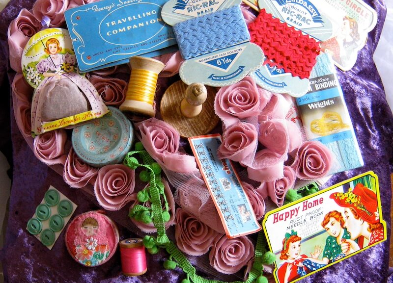 Grammar Guru: 12 Clever "Britishisms" to Adopt - 2 Assorted vintage sewing supplies and notions—like rickrack, buttons, thread spools, and fabric roses—are arranged on a purple cloth.
