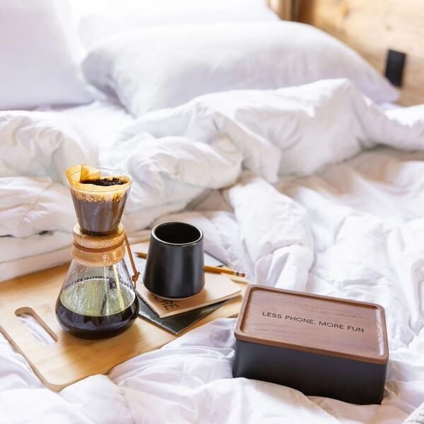 10 Digital Detox Destinations Around the South - 2 A tray on a rumpled bed holds a coffee carafe, a black cup, and a wooden box with the words “LESS PHONE. MORE FUN.”–a subtle invitation to embrace digital detox in one of the best places for relaxation.