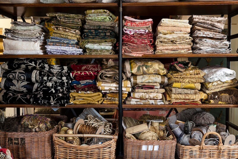Pillow Talk with B. Viz Design's Rebecca Vizard - 9 Shelves filled with neatly stacked colorful fabric and baskets below containing assorted sewing supplies such as thread, rope, and yarn create an organized space.
