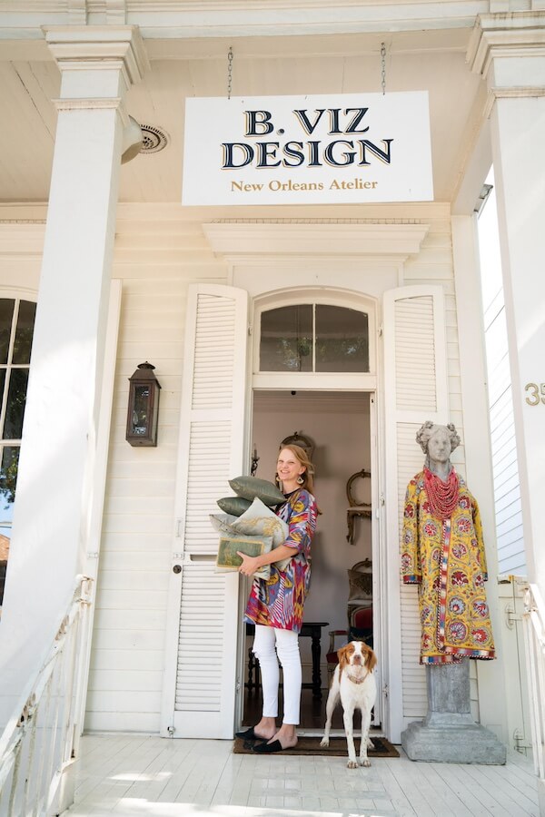 Pillow Talk with B. Viz Design's Rebecca Vizard - 7 A woman stands in the doorway of B. Viz Design New Orleans Atelier holding pillows, with a dog at her feet and a mannequin dressed in a colorful b. viz design robe beside her.