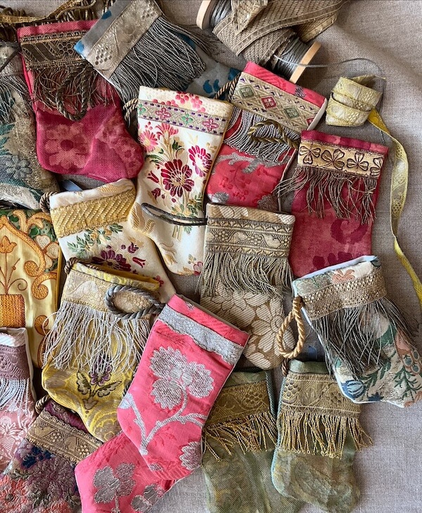 Pillow Talk with B. Viz Design's Rebecca Vizard - 10 A collection of ornate, vintage fabric stocking ornaments by b. viz design, featuring floral patterns, metallic trims, and fringe details arranged closely together.