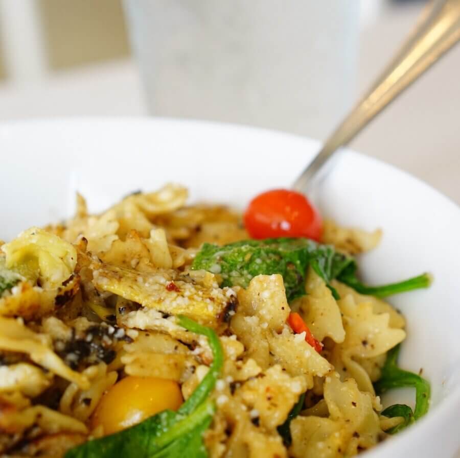 10 Ways to Spend New Year's Eve in Birmingham - 3 A white bowl filled with bow tie pasta, spinach, cherry tomatoes, and grated cheese sits ready to enjoy—perfect for a cozy New Year's Eve in Birmingham, with a fork resting inside.