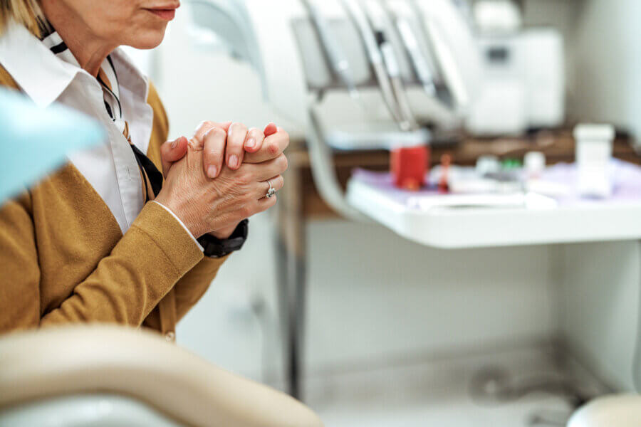 A person sits in a dental office with hands clasped, possibly waiting for a dental procedure. 