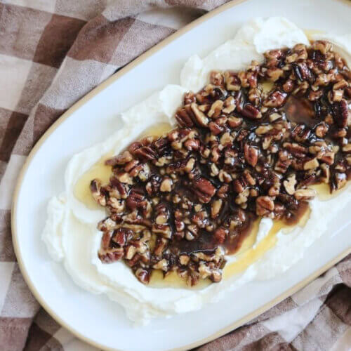 RECIPE: French Quarter Dip - 2 A serving platter with a layer of whipped cream cheese topped with chopped pecans and honey sits on a brown and white checkered cloth—perfect for easy appetizer recipes.