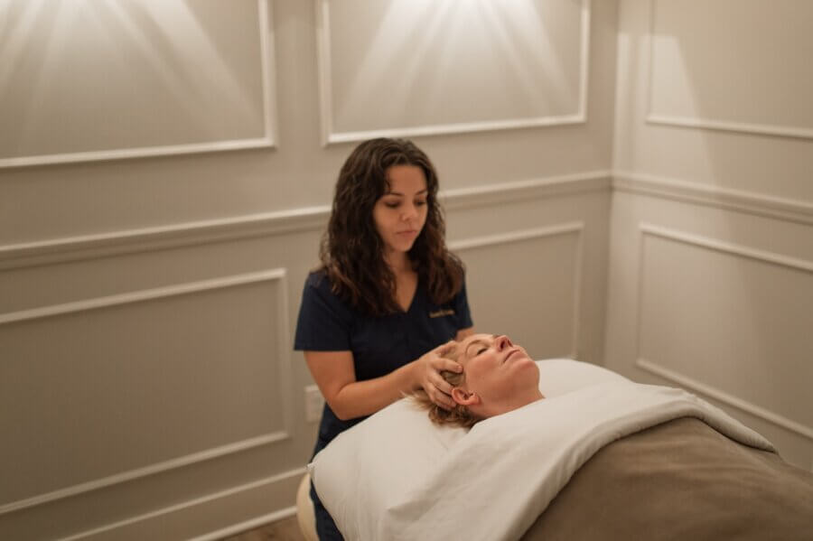 15 Decadent Nashville Spa Treatments to Gift - 4 A massage therapist gives a head massage to a person lying on a treatment table in a dimly lit spa room, creating the serene atmosphere that Nashville spas are known for.
