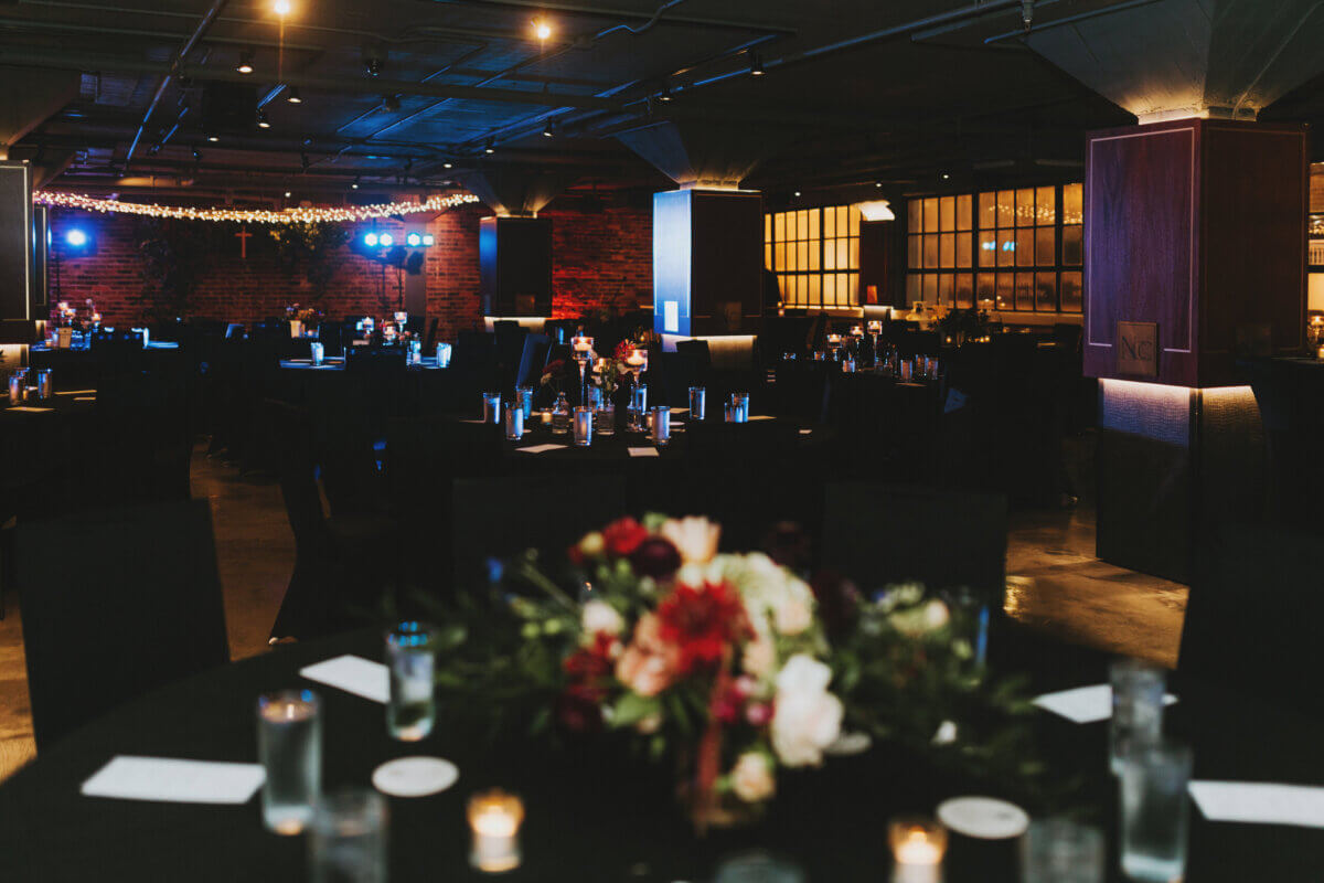 A dark Nashville event space featuring a banquet hall set with round tables, floral centerpieces, and candles.