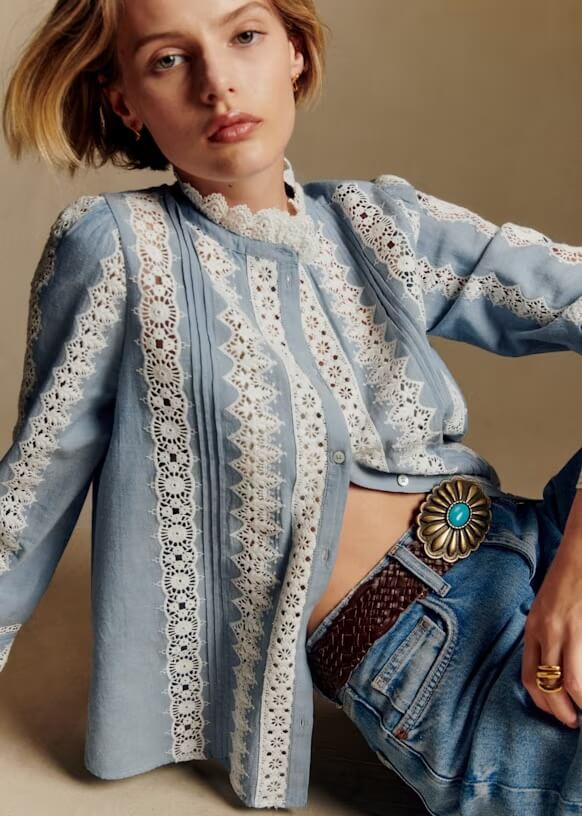 Trend Alert: Lace is Back! - 5 A person showcases a fashion trend alert in a light blue blouse with white Lace details, blue jeans, and a large belt with a turquoise stone buckle, seated against a neutral background.