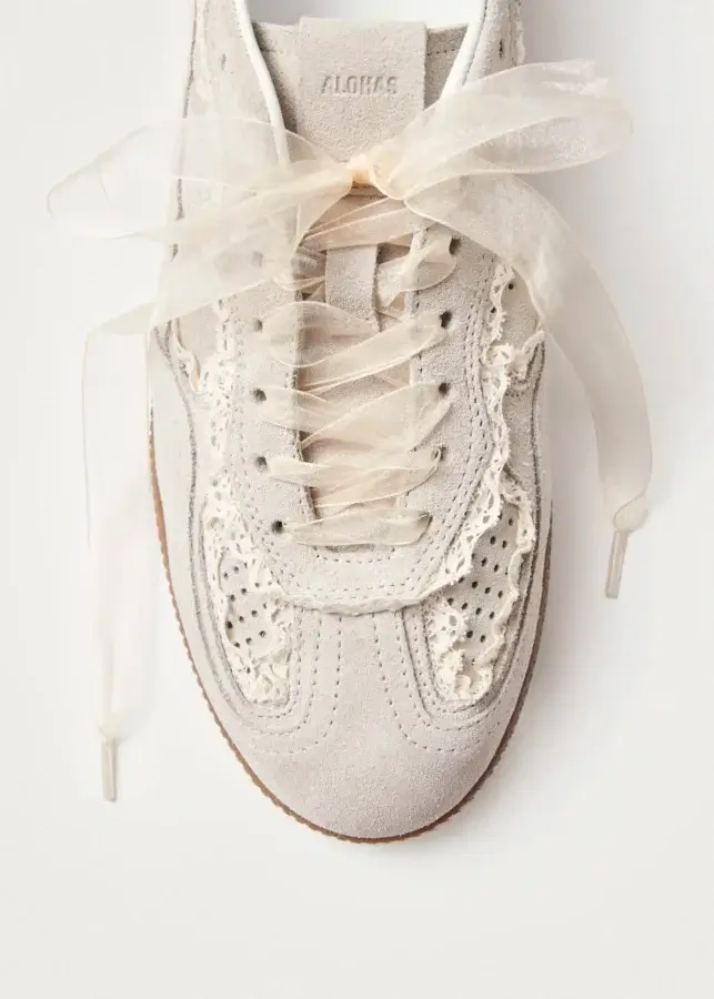 Trend Alert: Lace is Back! - 13 A beige suede sneaker with decorative lace details and sheer ribbon laces, viewed from above against a white background.