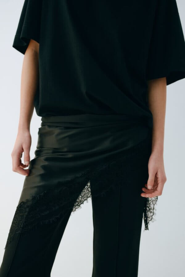 Trend Alert: Lace is Back! - 14 Trend Alert: Person wearing a loose black top and black skirt with lace detail layered over black pants, shown from shoulders to mid-thigh.