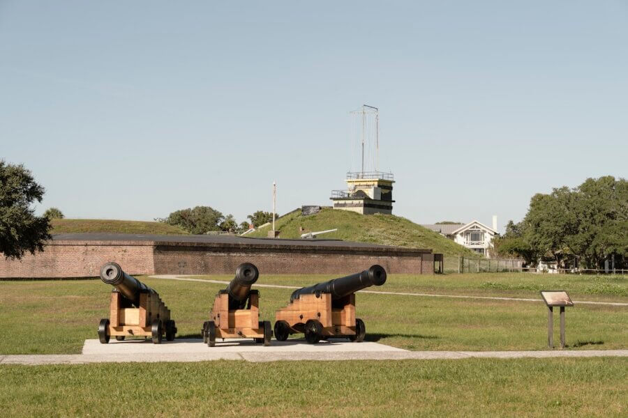 5 Must-Visit Lowcountry Attractions for Exploring Revolutionary History - 5 Three historic cannons on wooden carriages are displayed outdoors in front of a brick fort and grassy mound under a clear sky, making this site one of the notable Charleston attractions.