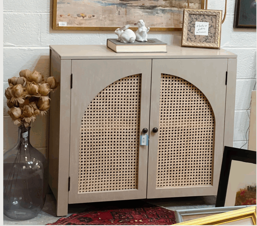 17 Birmingham FINDS for the New Year - 15 A beige cabinet with woven rattan doors sits against a wall, topped with books and decor—one of our favorite FINDS in Birmingham. Artworks and a large vase with dried flowers surround it, perfect for a fresh New Year look.
