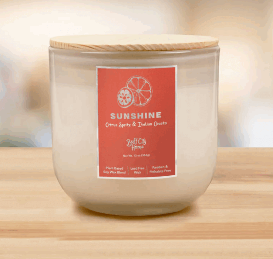 17 Birmingham FINDS for the New Year - 17 A white candle in a glass jar with a wooden lid. The label reads "Sunshine, Citrus Spritz & Italian Coasts, Buff City Home—Birmingham FINDS." Plant-based, lead-free, paraben- and phthalate-free—perfect for your New Year refresh.