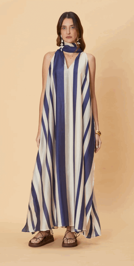 17 Birmingham FINDS for the New Year - 7 Woman stands against a beige background wearing a loose, sleeveless dress with wide blue and white diagonal stripes, a matching scarf, brown sandals, and gold bangles.