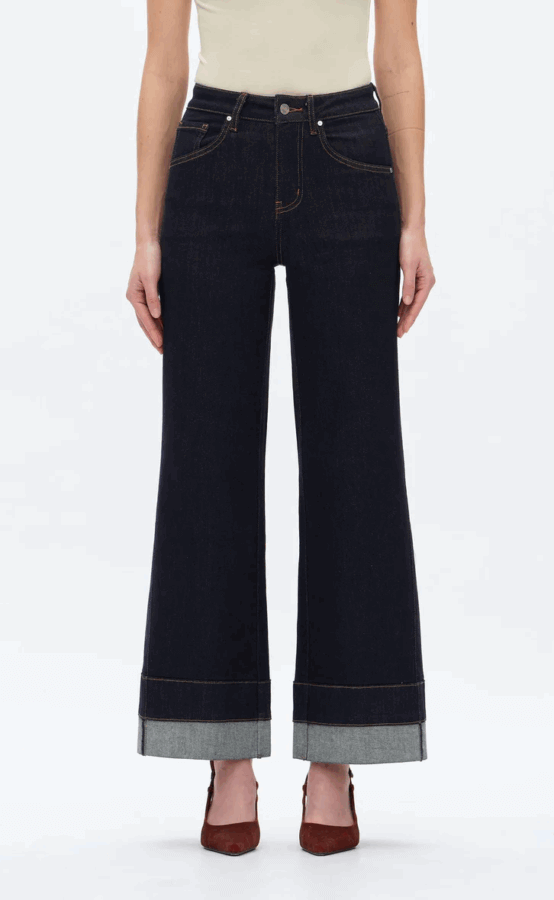 17 Birmingham FINDS for the New Year - 4 A person wearing high-waisted, dark wash wide-leg jeans with large cuffs, a light sleeveless top, and brown heels, standing against a plain white background.