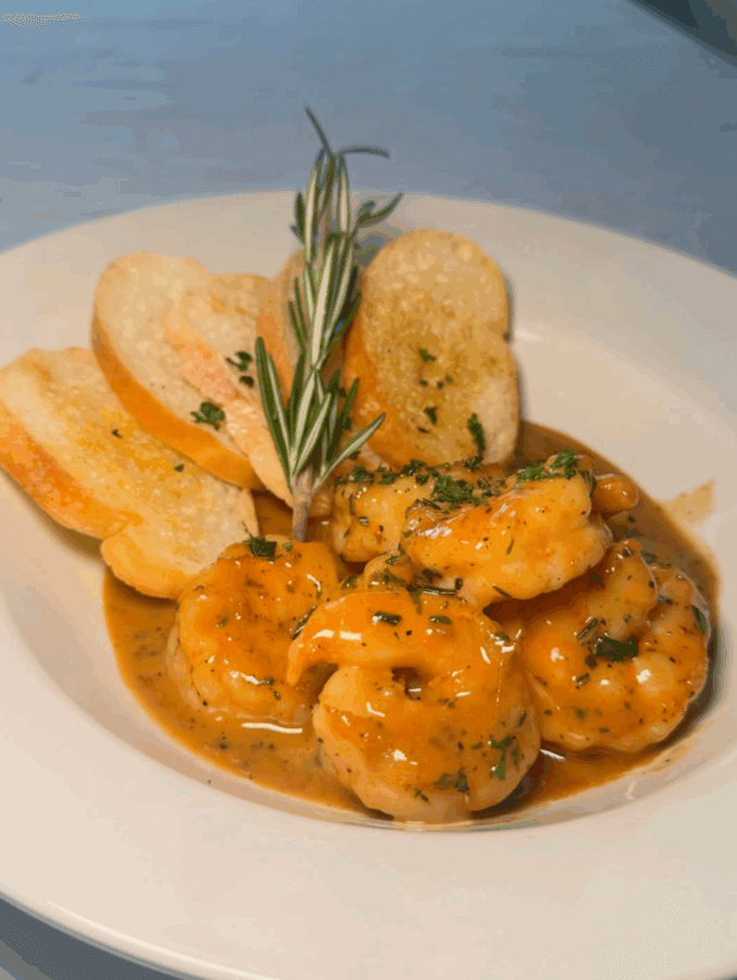 10 New Birmingham Restaurants to Try This Month - 23 Shrimp in a golden sauce garnished with herbs, served with toasted baguette slices and a sprig of rosemary—a delightful choice among Birmingham restaurants, perfect for those seeking exceptional Birmingham dining.