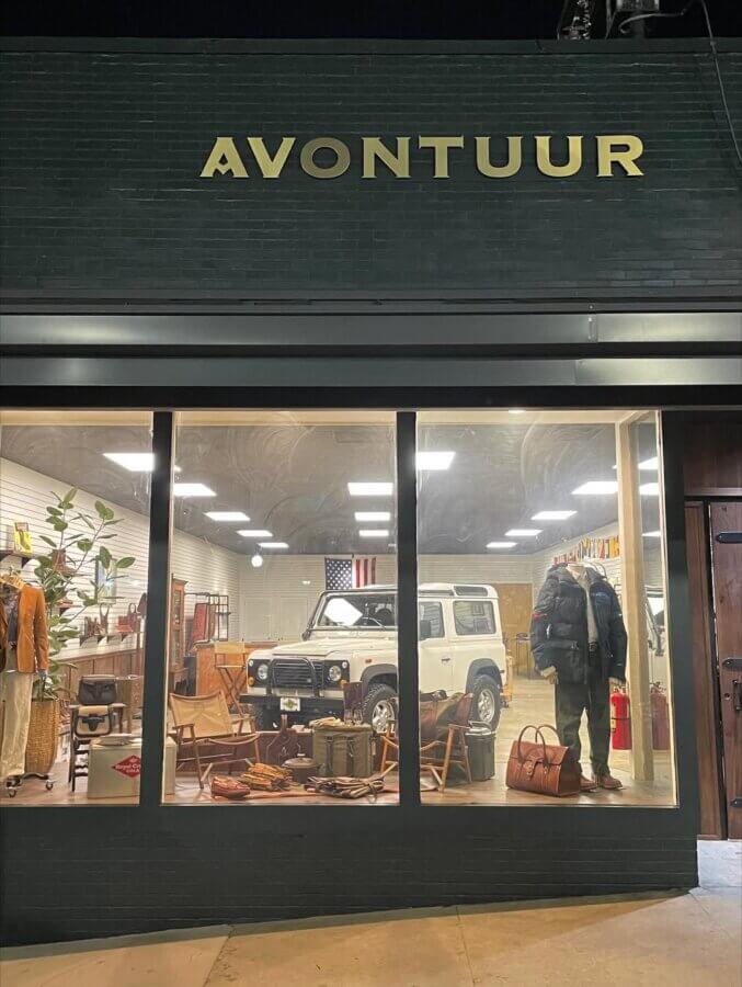 Avontuur: The New Homewood Shop You Need to Know - 8 Storefront of AVONTUUR, a Homewood specialty shop, with large windows displaying clothing, bags, and vintage items, with a white vintage Land Rover Defender vehicle in the center of the store.