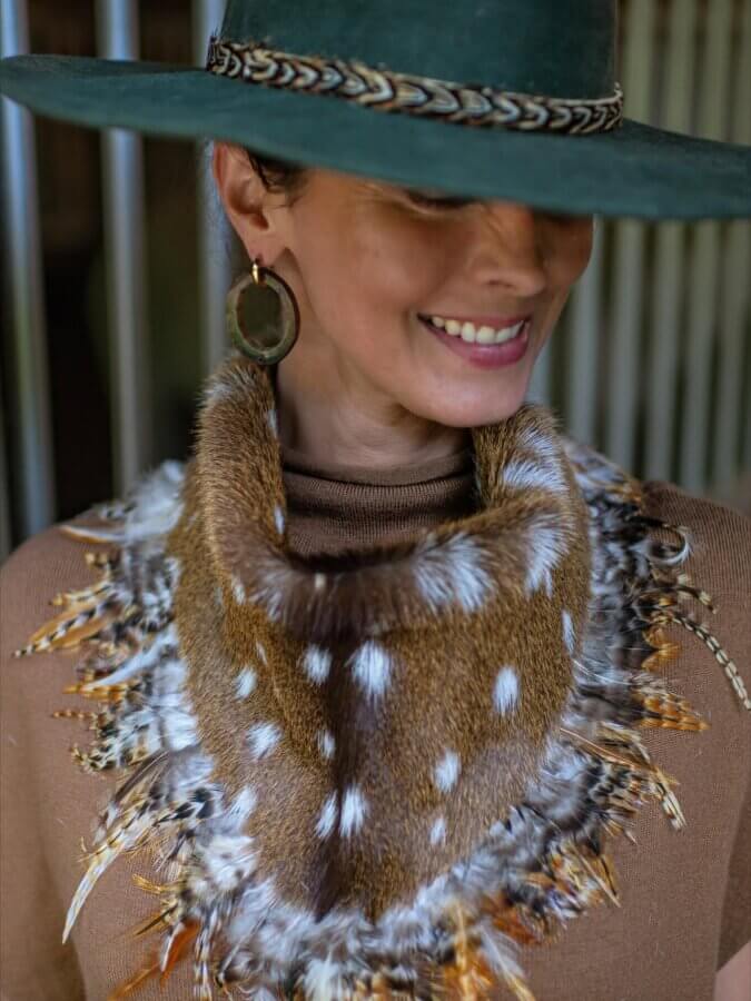 Avontuur: The New Homewood Shop You Need to Know - 9 Woman wearing a wide-brimmed green hat, brown top, statement earrings, and a fur and feather collar with spotted and striped patterns.