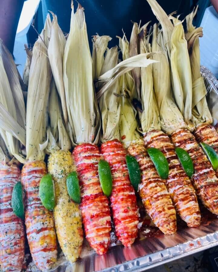 Aww Shucks! Meet the Woman Behind This Plant-Based BHAM Favorite - 4 A tray of grilled corn on the cob, covered in various seasonings and sauces, topped with lime wedges and husks attached for holding—a perfect plant-based food truck treat when you want to eat out and enjoy Southern food flavors.