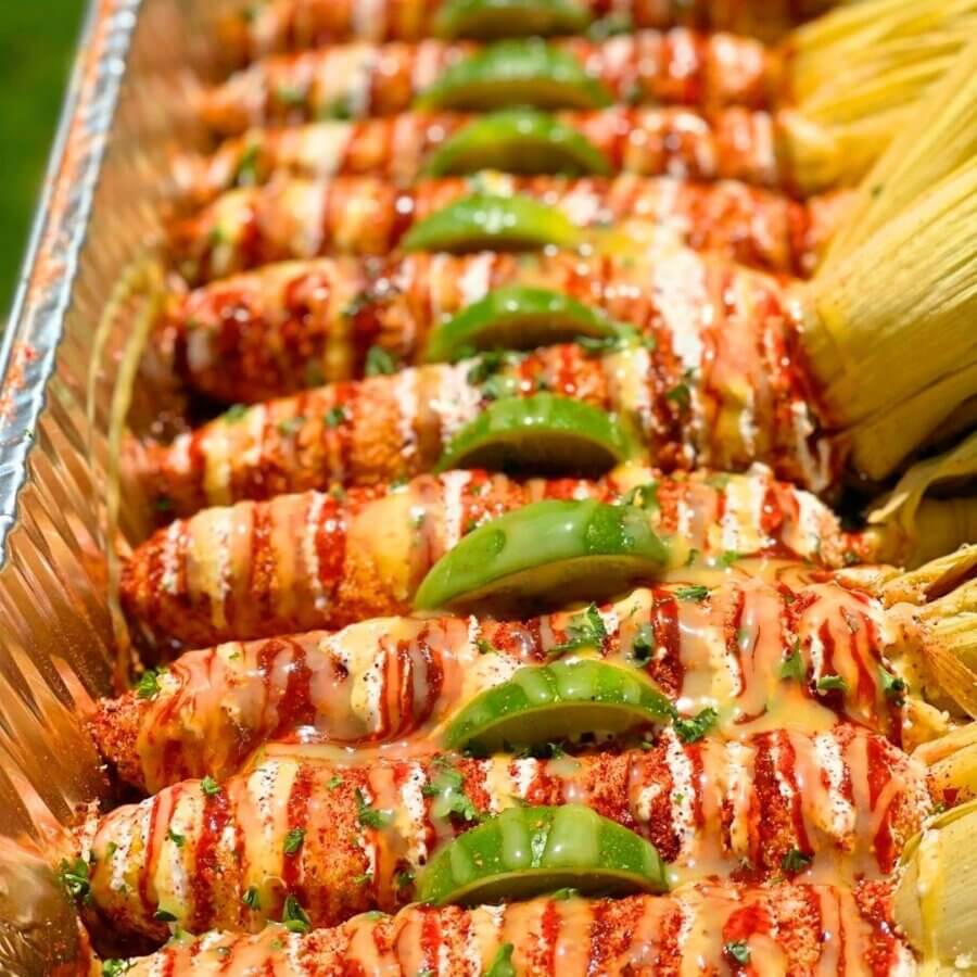 Aww Shucks! Meet the Woman Behind This Plant-Based BHAM Favorite - 7 A tray of elote corn on the cob topped with sauce, chili powder, cotija cheese, and lime wedges sits beside tamales—perfect for those looking to eat out and sample vibrant Southern cuisine.