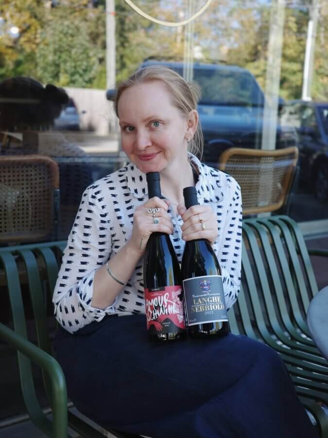 Kady Wohlfarth sits on a patio chair, smiling at the camera as she holds two bottles of Golden Age Wine—ready to share her favorite perfect pairings.