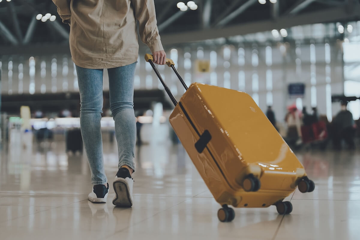 A person in jeans and sneakers pulls a yellow suitcase through an airport terminal, ready to travel and fly to their next destination.