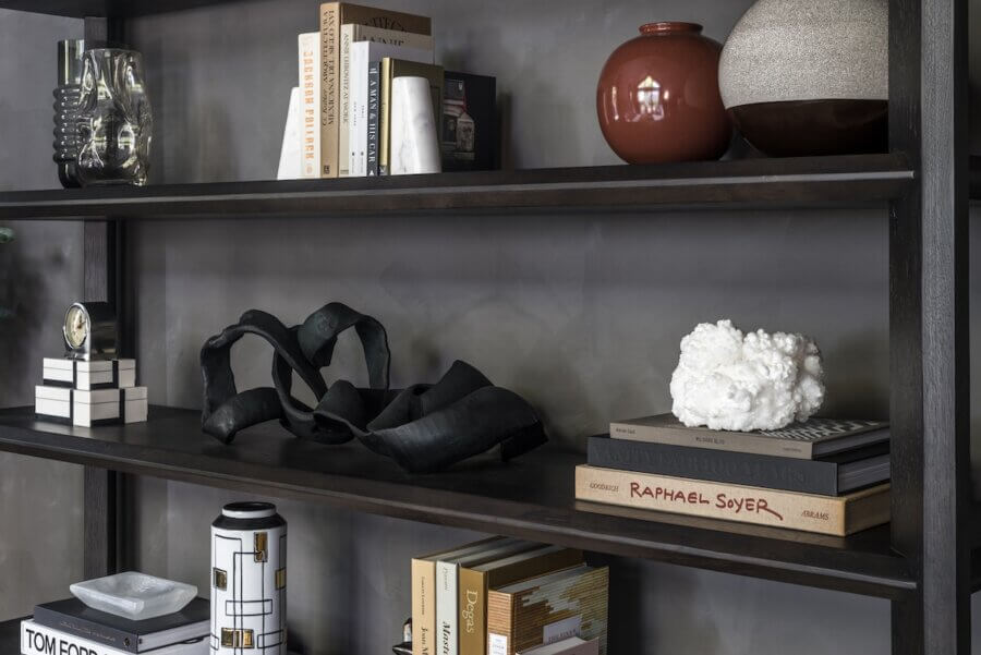 Dark wooden shelves showcase books, two ceramic vases, a white crystal cluster, a black abstract sculpture, a clock, and stylish decor—reflecting interior design trends 2026.