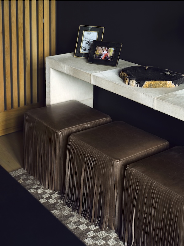 A white console table against a black wall holds framed photos and a decorative stone, while two brown leather fringe ottomans below reflect upcoming interior design trends 2026.