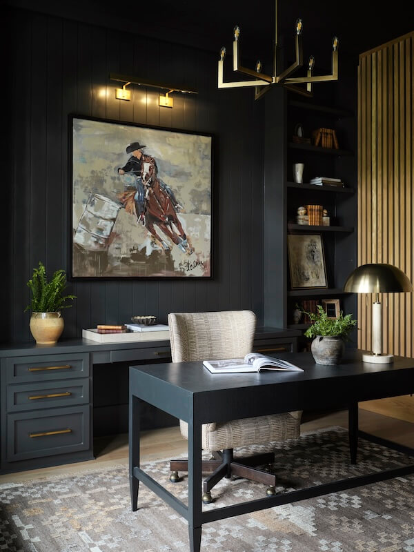 A modern home office with a black desk, beige chair, potted plants, wall art of a horse rider, built-in shelves, and gold-accented lighting showcases interior design trends 2026.