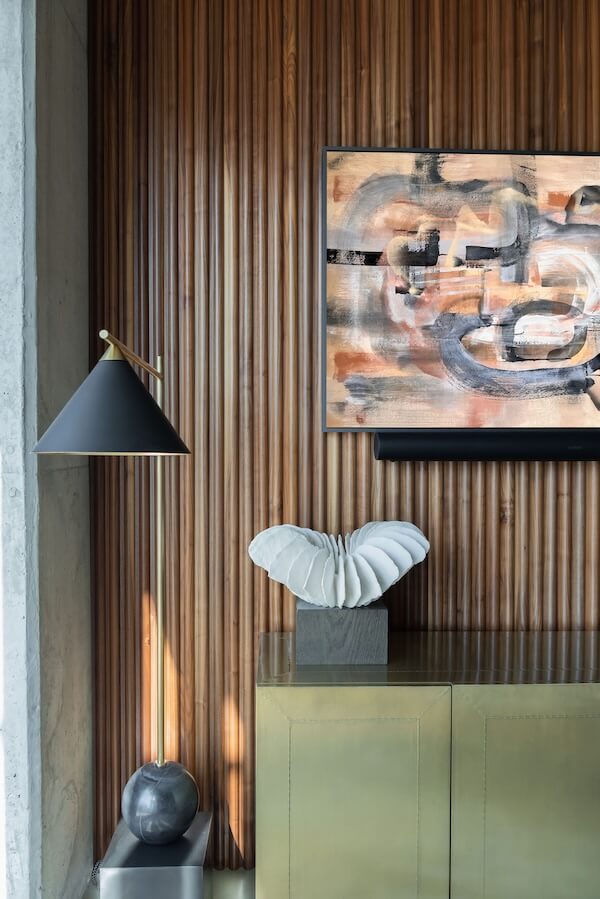 Modern interior with a ribbed wooden wall, abstract painting, black and gold floor lamp, brass cabinet, and white sculptural object—an elegant showcase of interior design trends 2026.