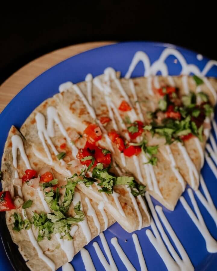 4 New Louisville Restaurants (+2 New Menus!) to Try This Month - 15 Three folded quesadillas topped with chopped cilantro, diced tomatoes, and drizzled with white sauce, served on a blue plate.