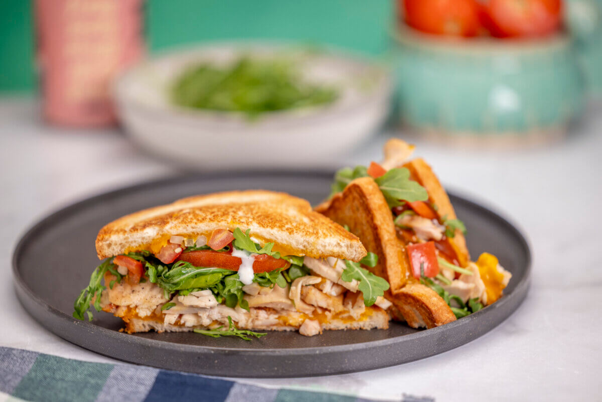 A toasted turkey sandwich with tomato, cheese, and arugula on a dark plate, as prepared by Memphis caterers.