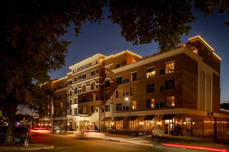 8 Mississippi Destinations Worth the Drive - 17 A four-story brick hotel with exterior lights illuminated at dusk, showing arched windows, a main entrance, and cars passing byβa charming highlight among Mississippi destinations.