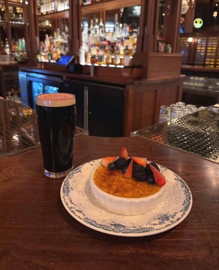 13 Spots to Grab Dinner at the Bar in Memphis - 2 Enjoy dinner at the bar with a pint of dark beer and a crΓ¨me brΓ»lΓ©e topped with berries, set on a wooden table in one of Memphisβ best spots, surrounded by bottles and glassware.