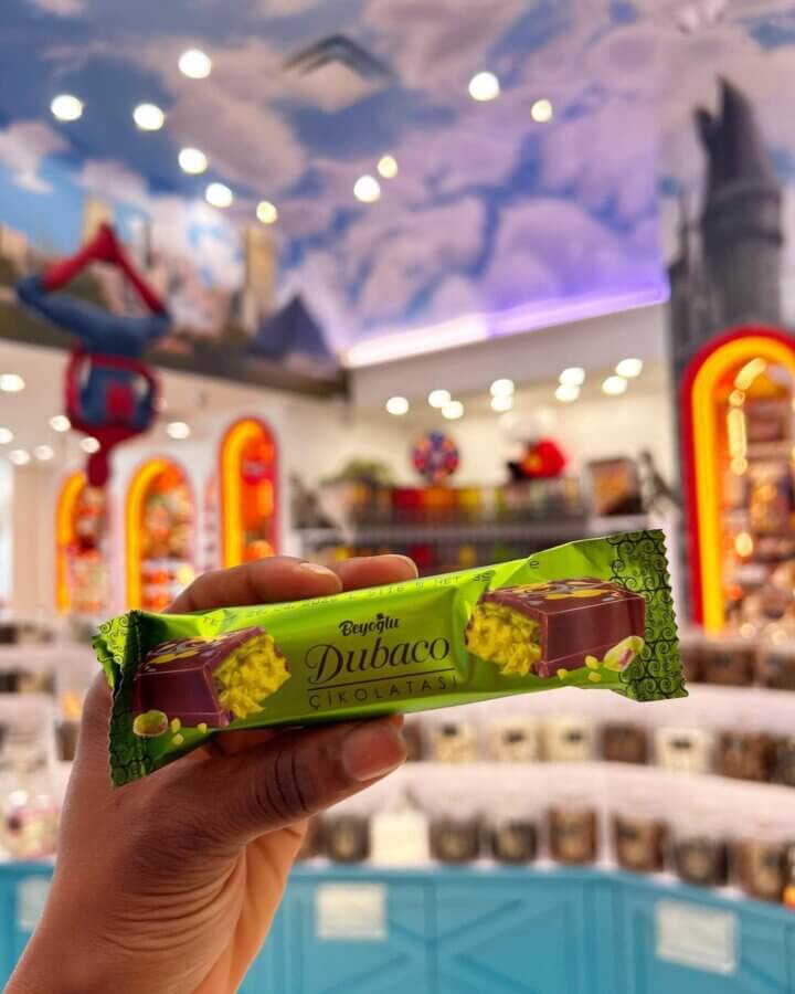 7 Best Candy Shops in Memphis (+ One Local Fave You Can Shop Online) - 7 A hand holds a Dubaco chocolate bar in one of the best candy shops in Memphis, surrounded by colorful jars and a painted sky ceiling.