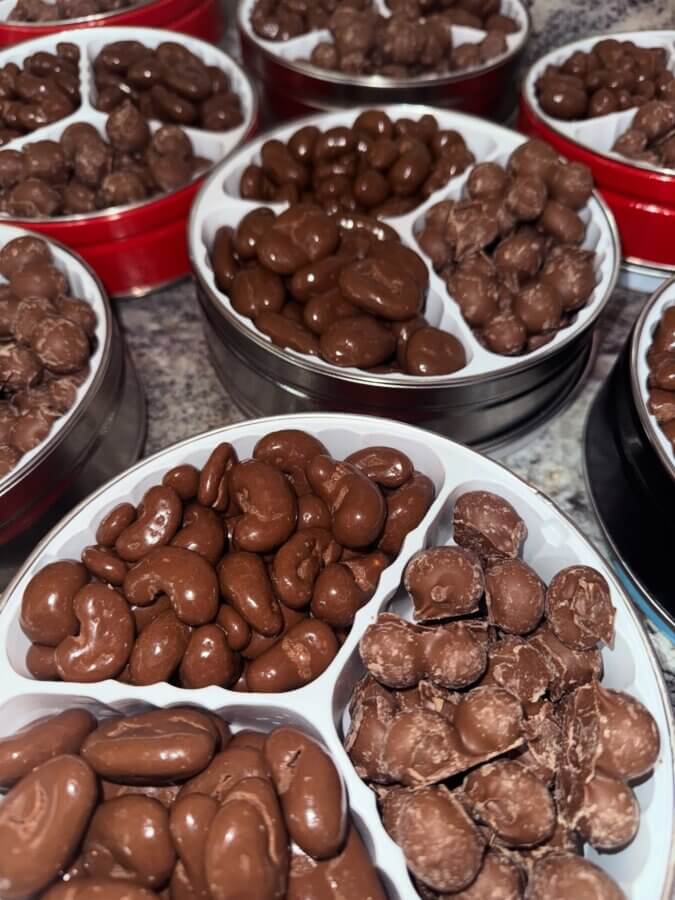 7 Best Candy Shops in Memphis (+ One Local Fave You Can Shop Online) - 5 Several round tins filled with assorted chocolate-covered nuts and candies, reminiscent of Memphis candy shops, are arranged on a countertop—perfect for gifting.
