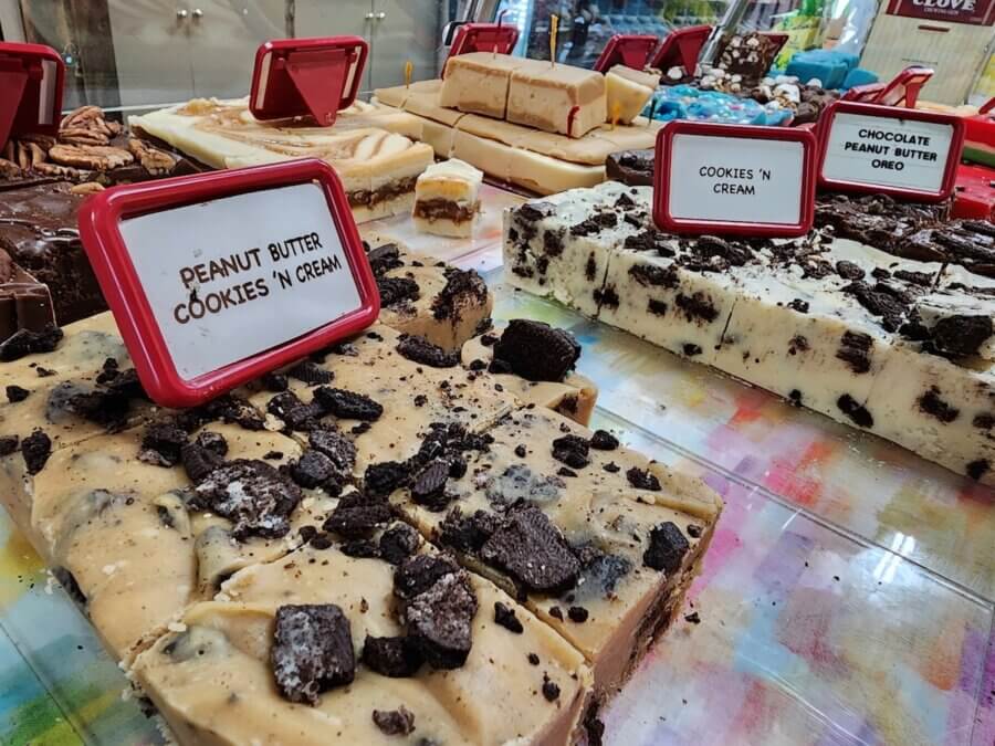 7 Best Candy Shops in Memphis (+ One Local Fave You Can Shop Online) - 2 Assorted fudge blocks, including peanut butter cookies 'n cream and cookies 'n cream flavors, are displayed on a clear counter with labeled signs from one of the best candy shops in Memphis.