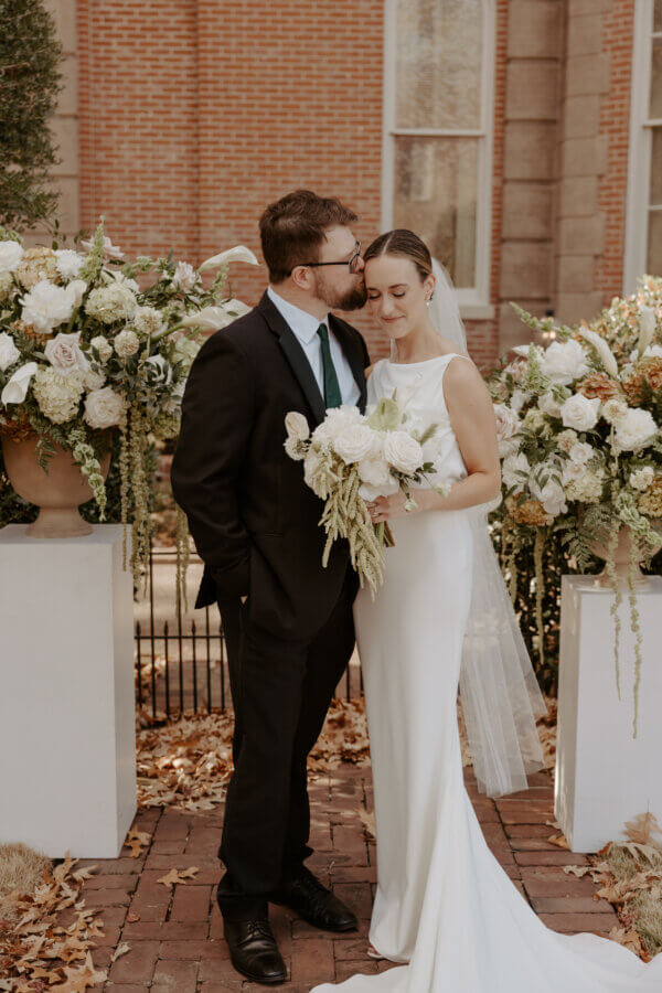 An Elegant Memphis Wedding at The Historic James Lee House - 10 A groom kisses his bride on the temple as she holds her wedding bouquet.