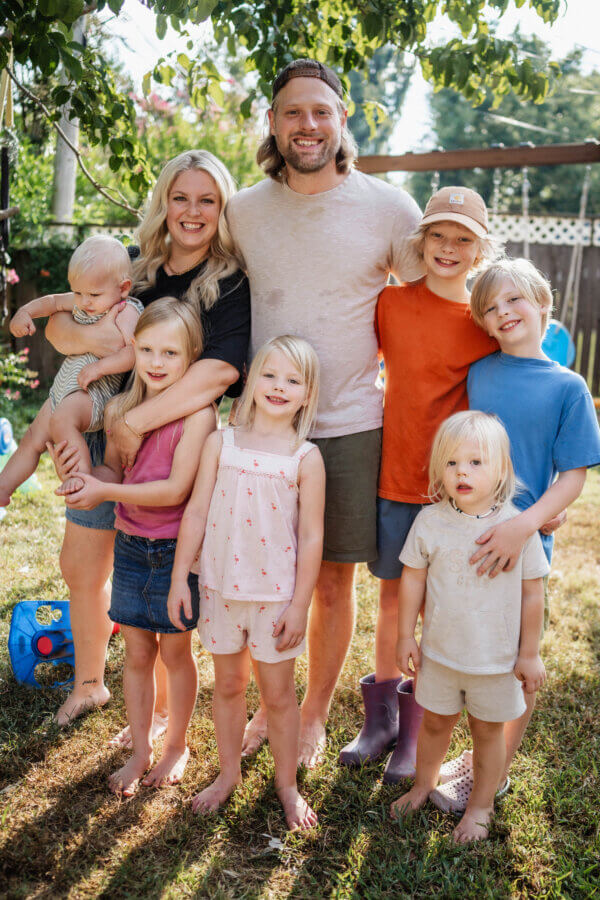 Meet Jasmin Day of Ease Wellness & JDay Bakes - 5 A family of seven poses barefoot in a backyard for Jasmin Day, with two adults and five children smiling at the camera on a sunny day, their FACES beaming with joy.