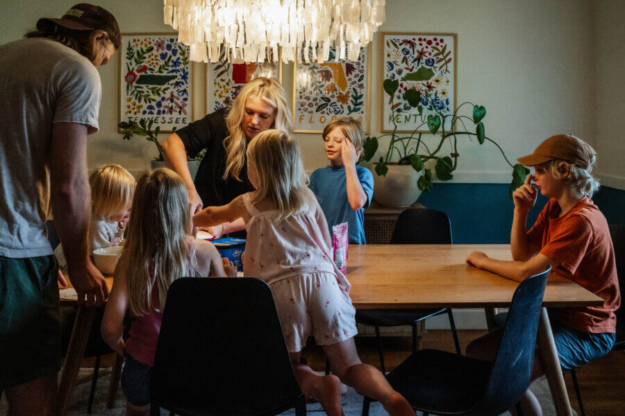 Meet Jasmin Day of Ease Wellness & JDay Bakes - 7 A group of children and two adults gather around a dining table with snacks and games under a chandelier in a brightly decorated room, enjoying laughter and fun on Jasmin Day.