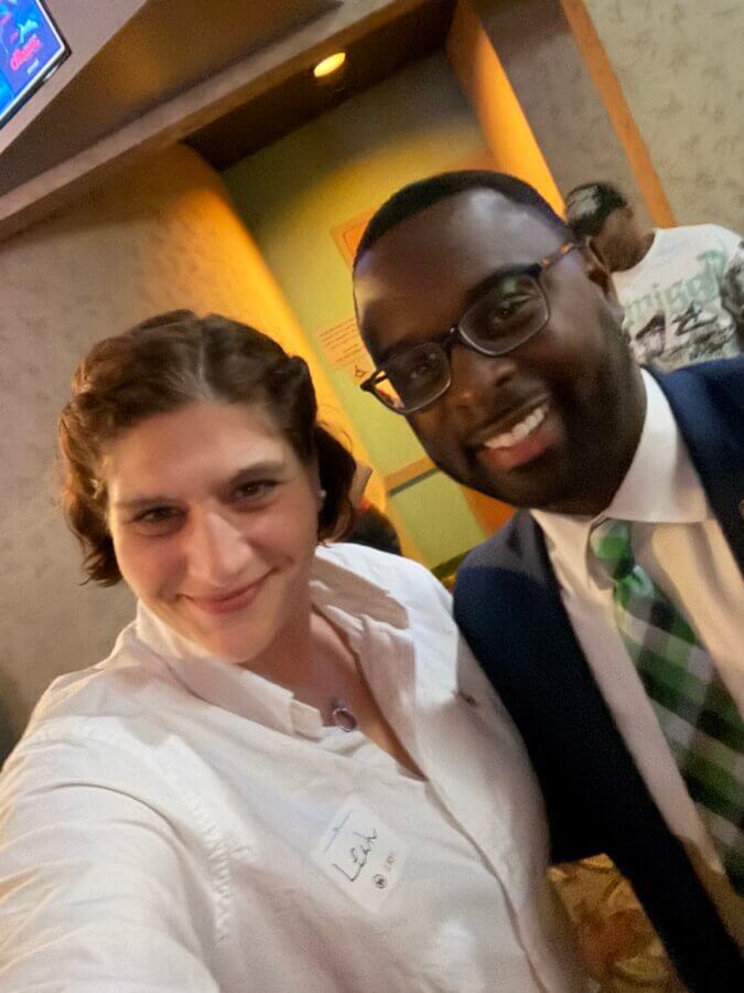 Honoring the 1.5 Million: Leah Fox-Greenberg and the Mission of the Unknown Child Foundation - 3 Two people are standing indoors, smiling at the camera. The person on the left wears a white shirt; the person on the right wears glasses, a suit, and a green striped tie.