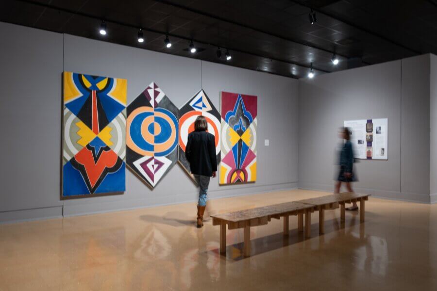 The Unexpected Side of Jackson, MS: Best Museums, Neighborhoods & Restaurants to Explore - 5 Two people view colorful abstract paintings displayed on a gray wall in an art gallery, with a wooden bench positioned in front of the artworks, highlighting the vibrant culture found in Jackson museums.