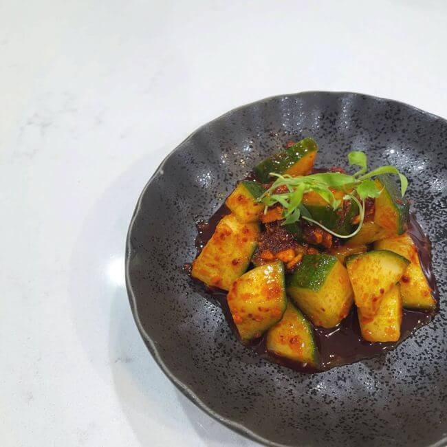 5 New Memphis Restaurants to Try This Month (+ What's Coming Soon!) - 14 A black bowl containing spicy marinated cucumber pieces garnished with microgreens, this dish is a fresh favorite at new Memphis restaurants, served on a pristine white surface.