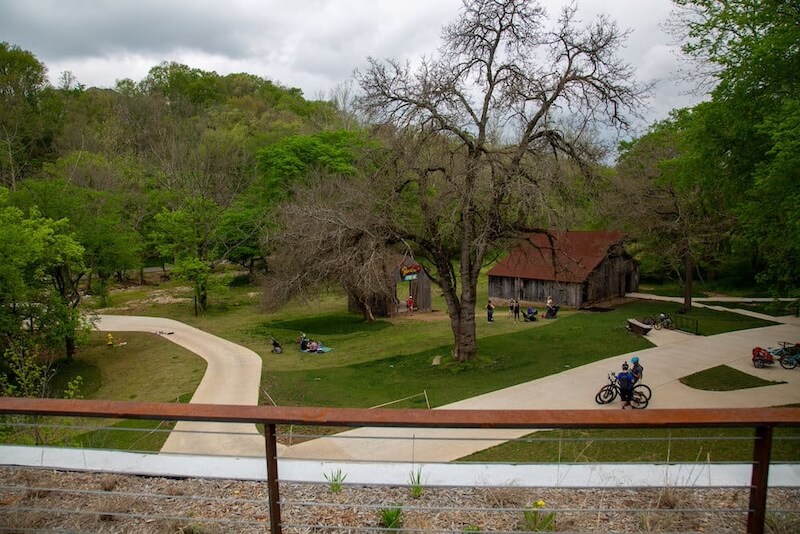 8 Adventurous Girls' Trips (All Skill Levels!) - 8 View of a park with winding paths, scattered groups of people, lush green trees, and a rustic wooden building under a cloudy sky—an ideal spot for adventurous girls trips.