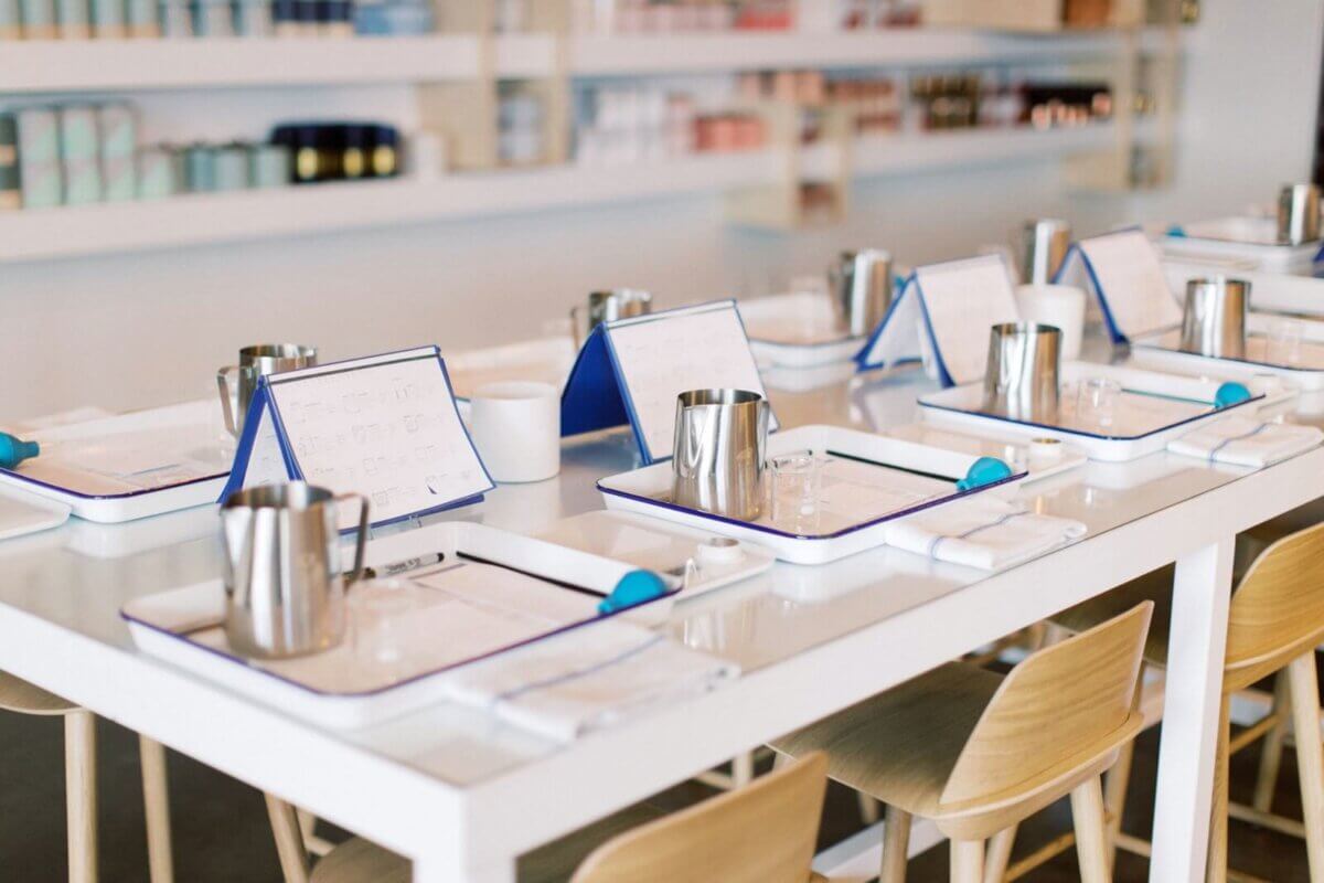 A clean, modern table is set with metal pitchers, trays, menus, and utensils in a brightly lit room—perfect for a Nashville Adult Education workshop, with shelves stocked in the background.