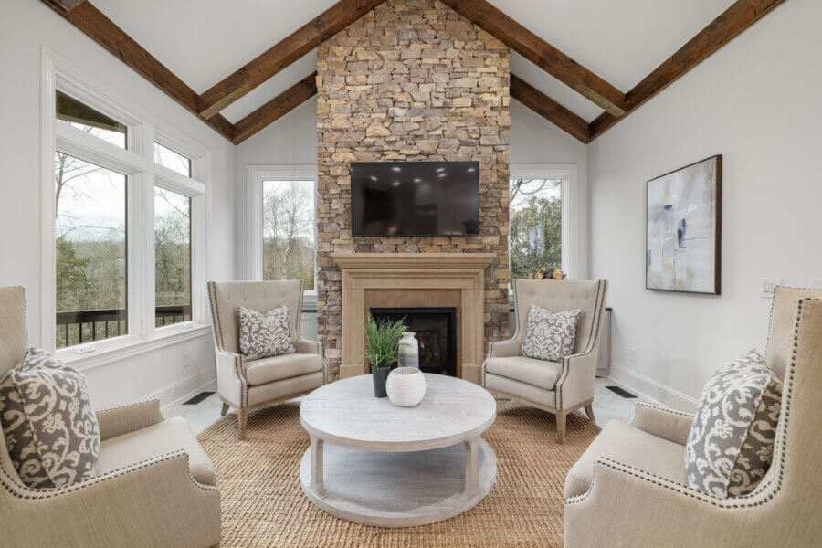 Just Listed! A Franklin Home Designed to Entertain & Unwind - 9 Just Listed! Entertain guests in this Franklin Home's inviting living room, featuring four beige armchairs around a round coffee table, a stone fireplace with TV above, large windows, and elegant neutral décor.